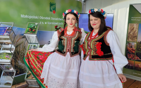 Na zdjęciu na zdjęciu widoczna są dwie panie w strojach ludowych zapraszające na stanowisko małopolskiego ośrodka doradztwa rolniczego