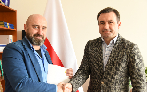 Na zdjęciu dyrektor wodr i prezes somatik stoją ze ściśniętymi dłońmi przed flagą polski po podpisaniu umowy sponsorskiej.