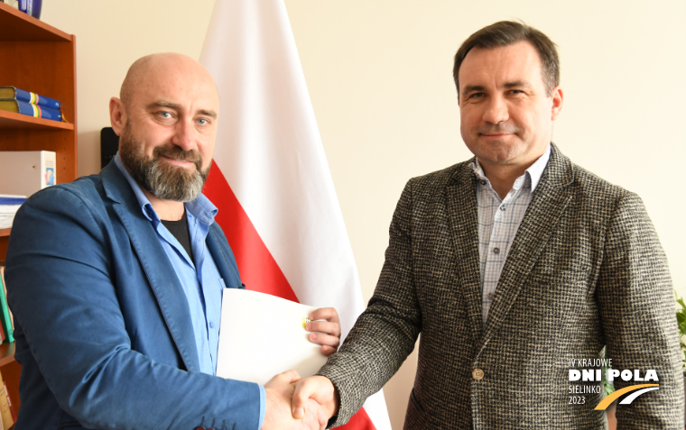 Na zdjęciu dyrektor wodr i prezes somatik stoją ze ściśniętymi dłońmi przed flagą polski po podpisaniu umowy sponsorskiej.